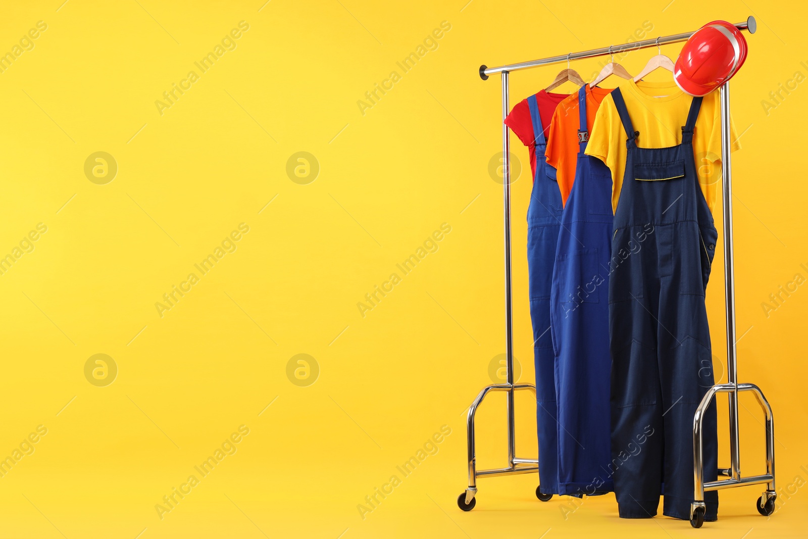 Photo of Workers' uniforms on clothing rack against yellow background. Space for text