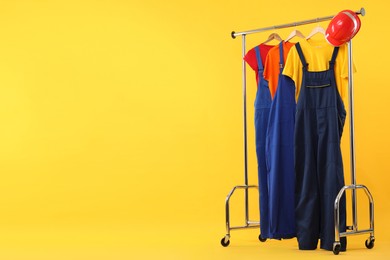 Photo of Workers' uniforms on clothing rack against yellow background. Space for text