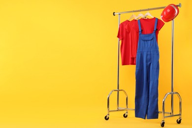 Photo of Workers' uniform and t-shirts on clothing rack against yellow background. Space for text