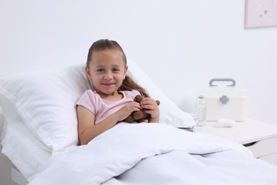 Cute little girl with teddy bear on bed in hospital