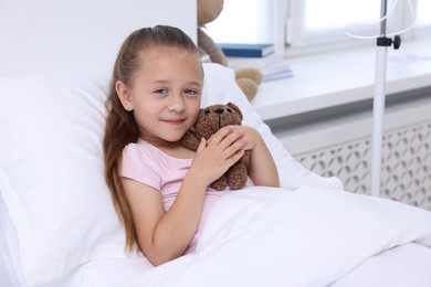 Cute little girl with teddy bear on bed in hospital