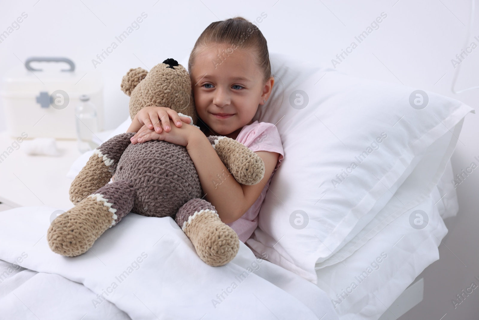 Photo of Cute little girl with teddy bear on bed in hospital