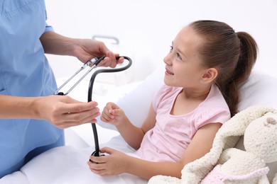 Photo of Doctor examining little girl on bed at hospital, closeup