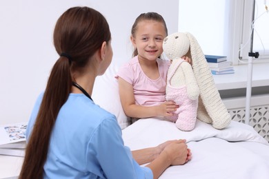 Photo of Doctor examining little girl on bed at hospital