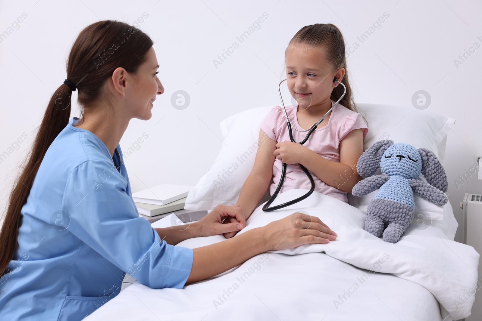 Photo of Doctor examining little girl on bed at hospital