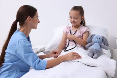 Doctor examining little girl on bed at hospital