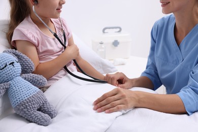 Photo of Doctor examining little girl on bed at hospital, closeup