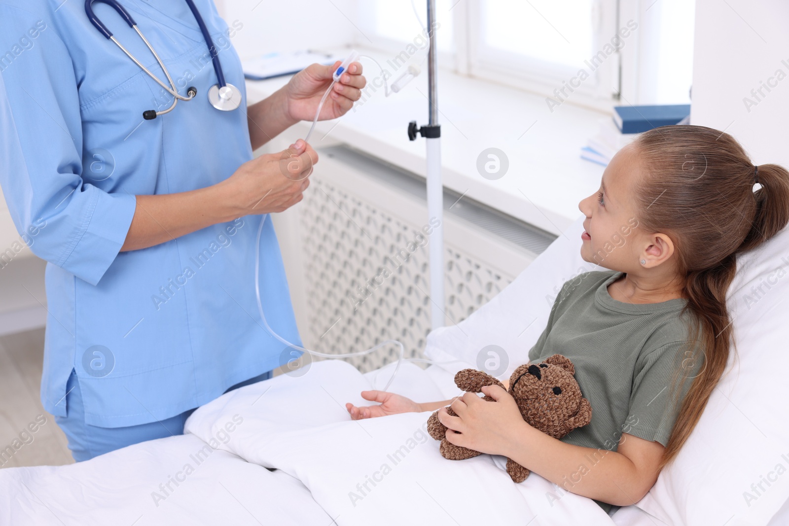 Photo of Doctor examining little girl and setting IV drip on bed at hospital, closeup