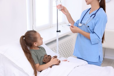 Doctor examining little girl and setting IV drip on bed at hospital, closeup