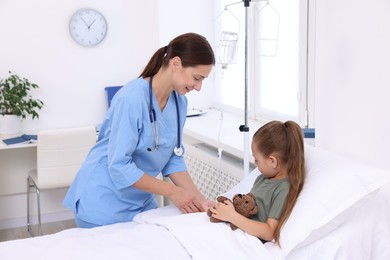 Doctor examining little girl and setting IV drip on bed at hospital