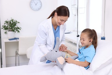 Doctor examining little girl on bed at hospital