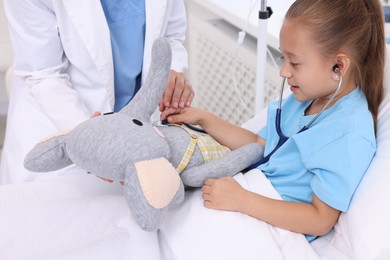 Doctor examining little girl on bed at hospital, closeup