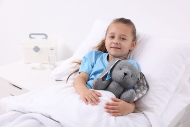 Cute little girl with toy bunny on bed in hospital