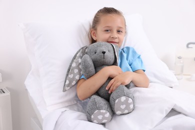 Cute little girl with toy bunny on bed in hospital