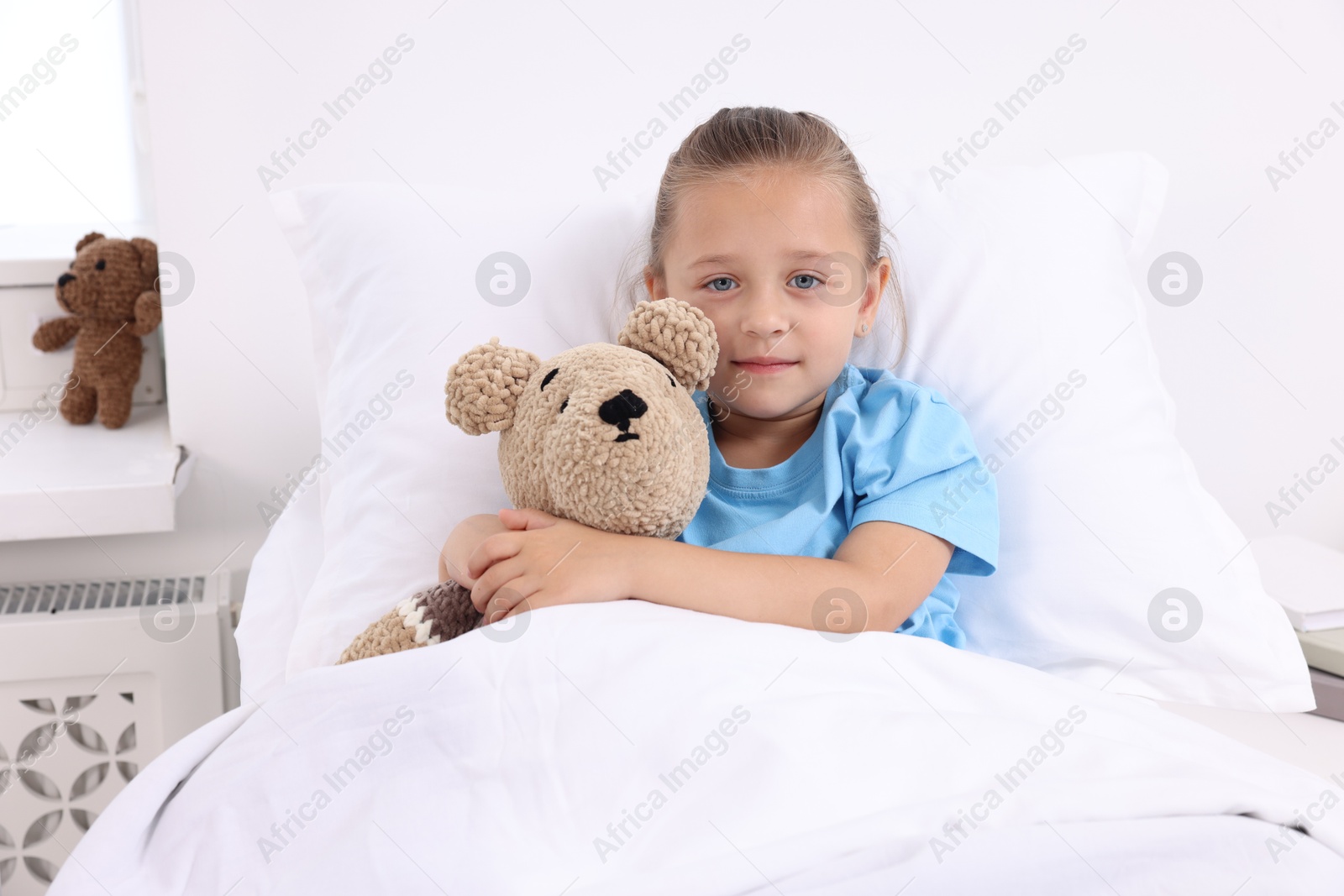 Photo of Cute little girl with teddy bear on bed in hospital