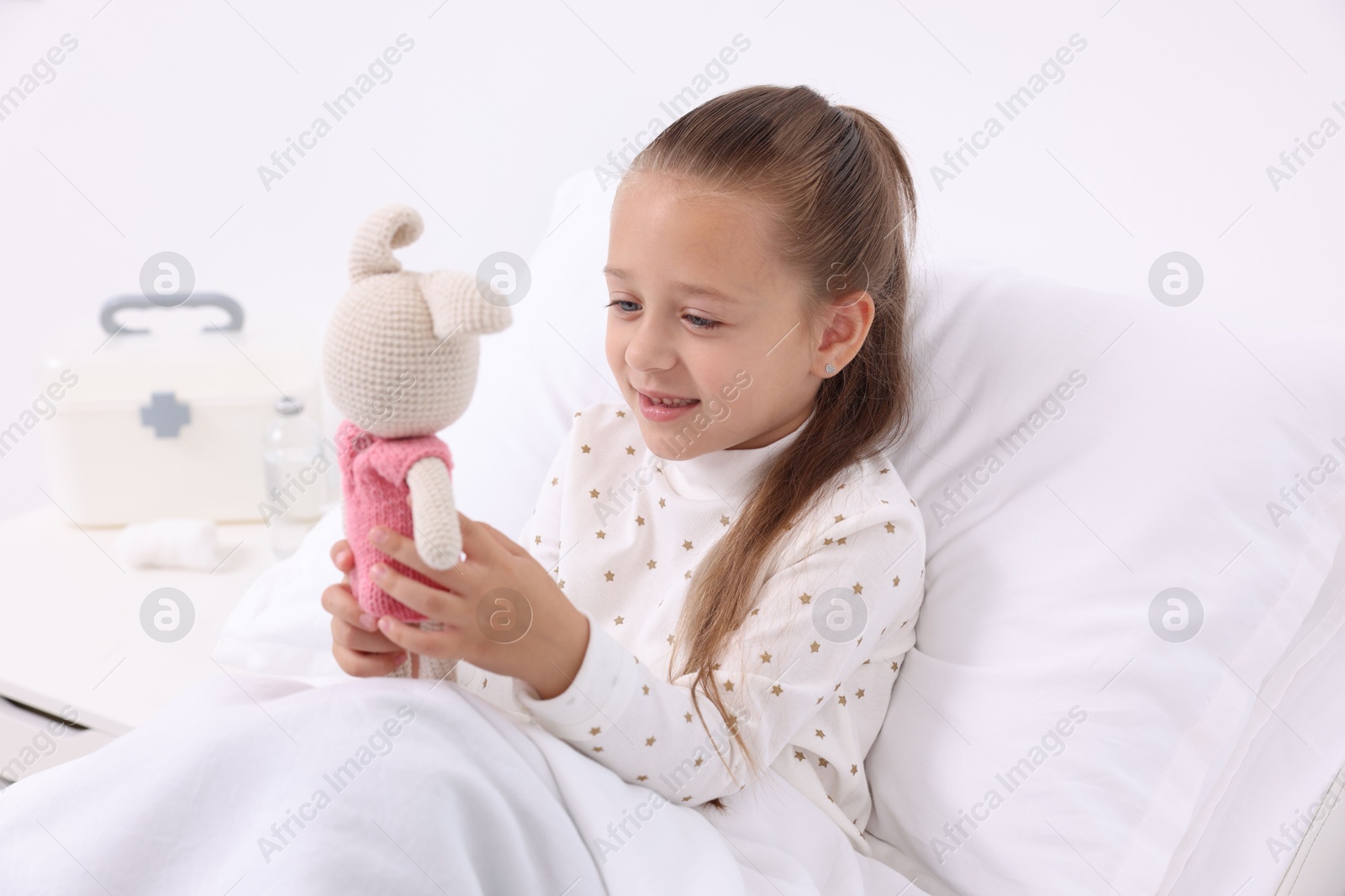 Photo of Cute little girl with toy bunny on bed in hospital