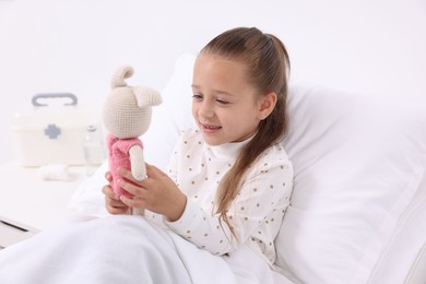 Cute little girl with toy bunny on bed in hospital