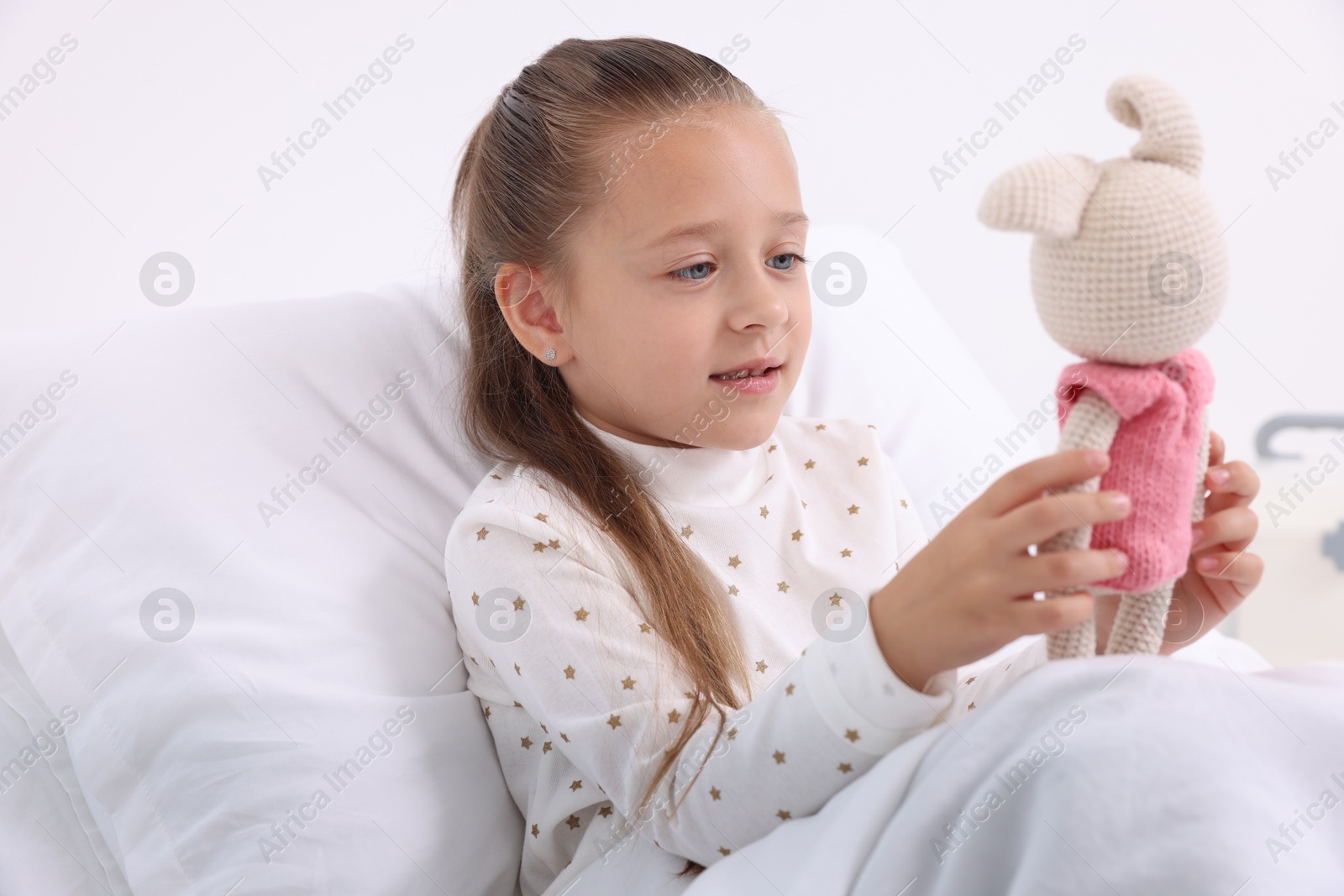 Photo of Cute little girl with toy bunny on bed in hospital