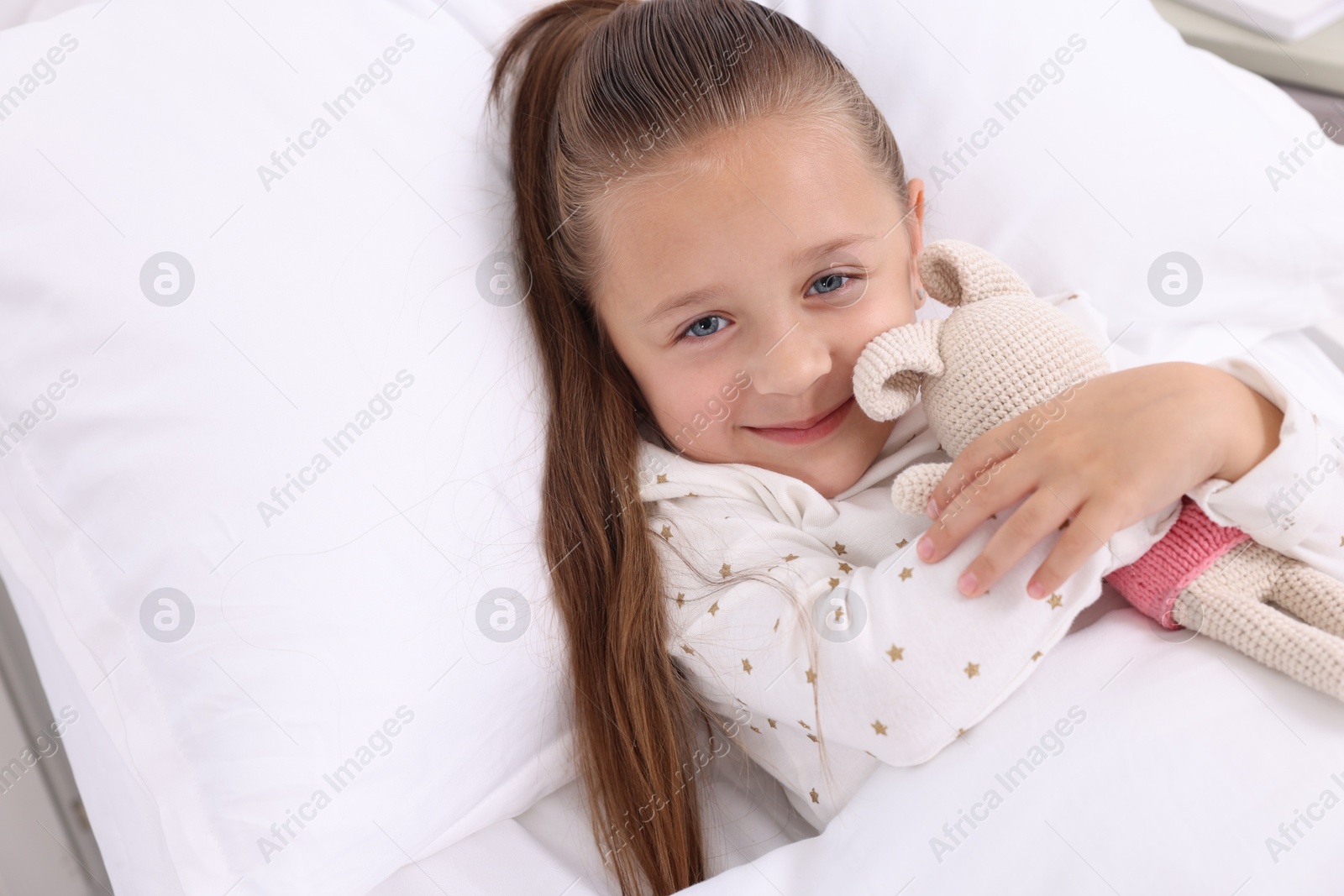 Photo of Cute little girl with toy bunny on bed in hospital