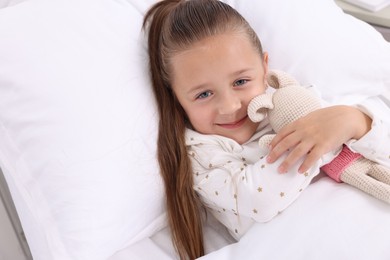 Photo of Cute little girl with toy bunny on bed in hospital