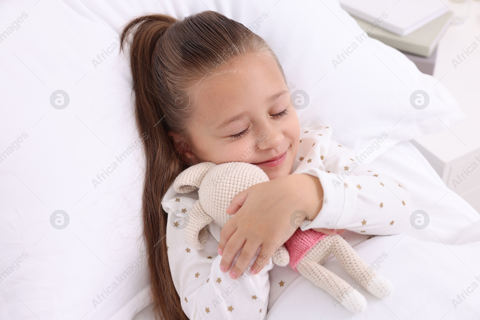 Photo of Cute little girl with toy bunny on bed in hospital