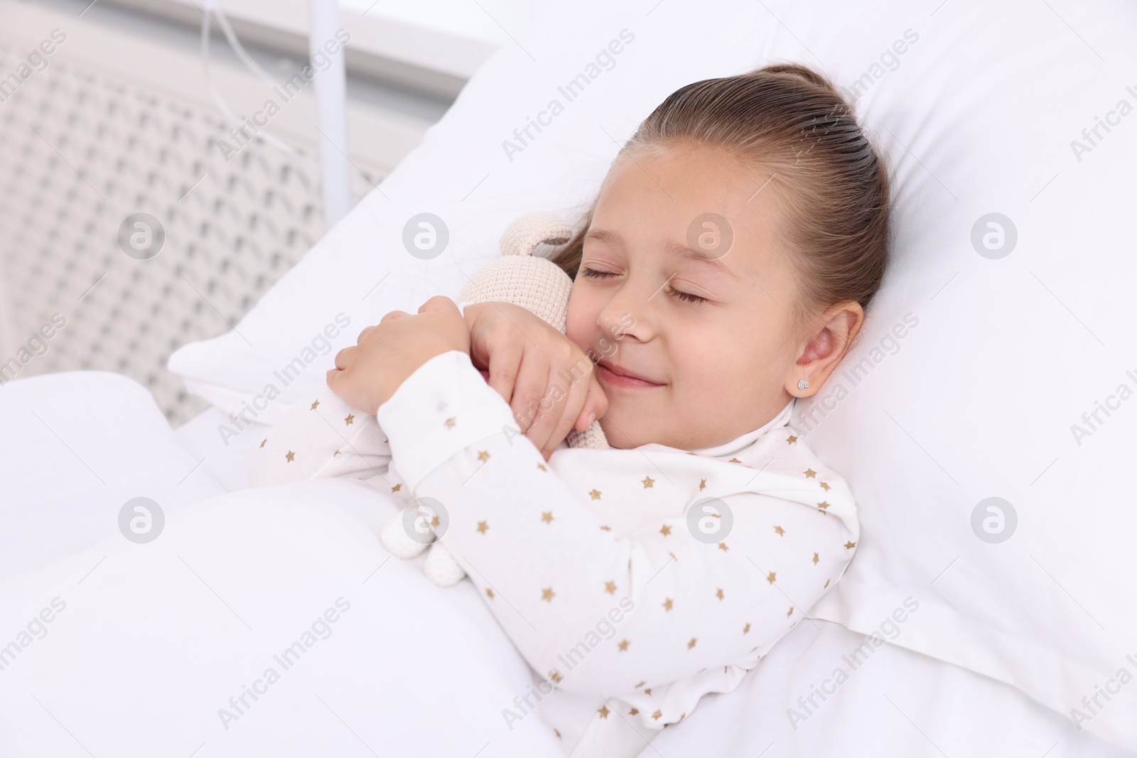 Photo of Cute little girl with toy bunny on bed in hospital