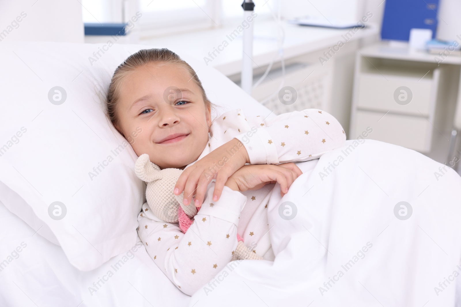 Photo of Cute little girl with toy bunny on bed in hospital