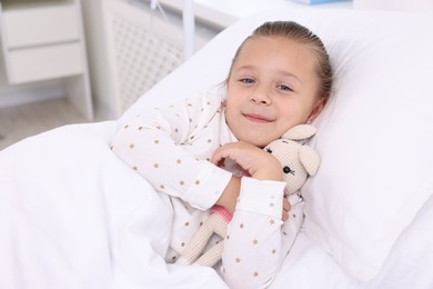 Cute little girl with toy bunny on bed in hospital