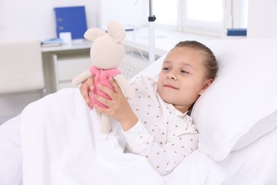 Cute little girl with toy bunny on bed in hospital