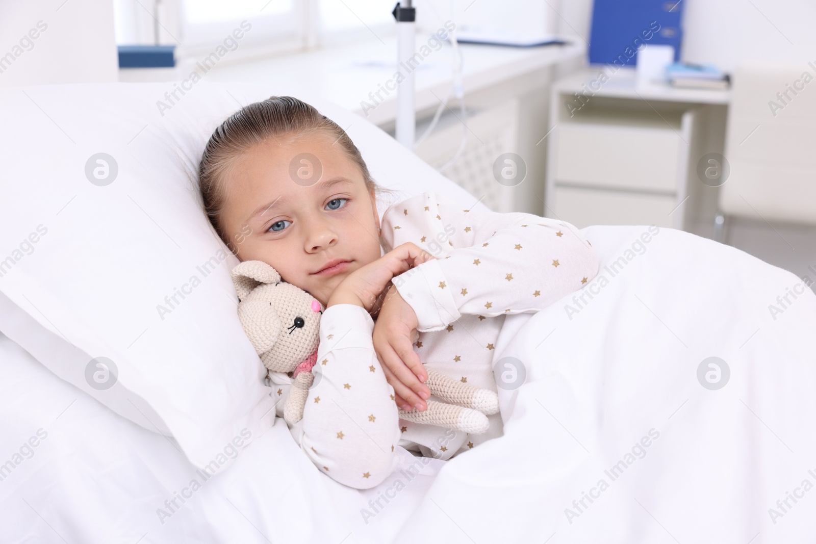 Photo of Cute little girl with toy bunny on bed in hospital