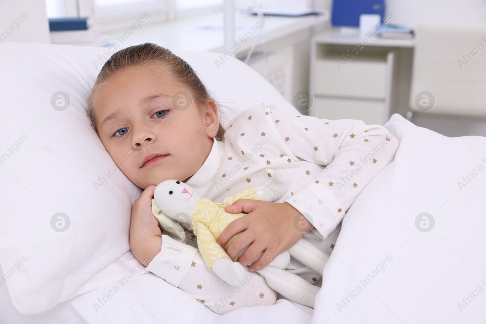 Photo of Cute little girl with toy bunny on bed in hospital