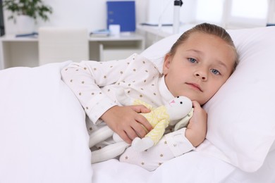 Photo of Cute little girl with toy bunny on bed in hospital