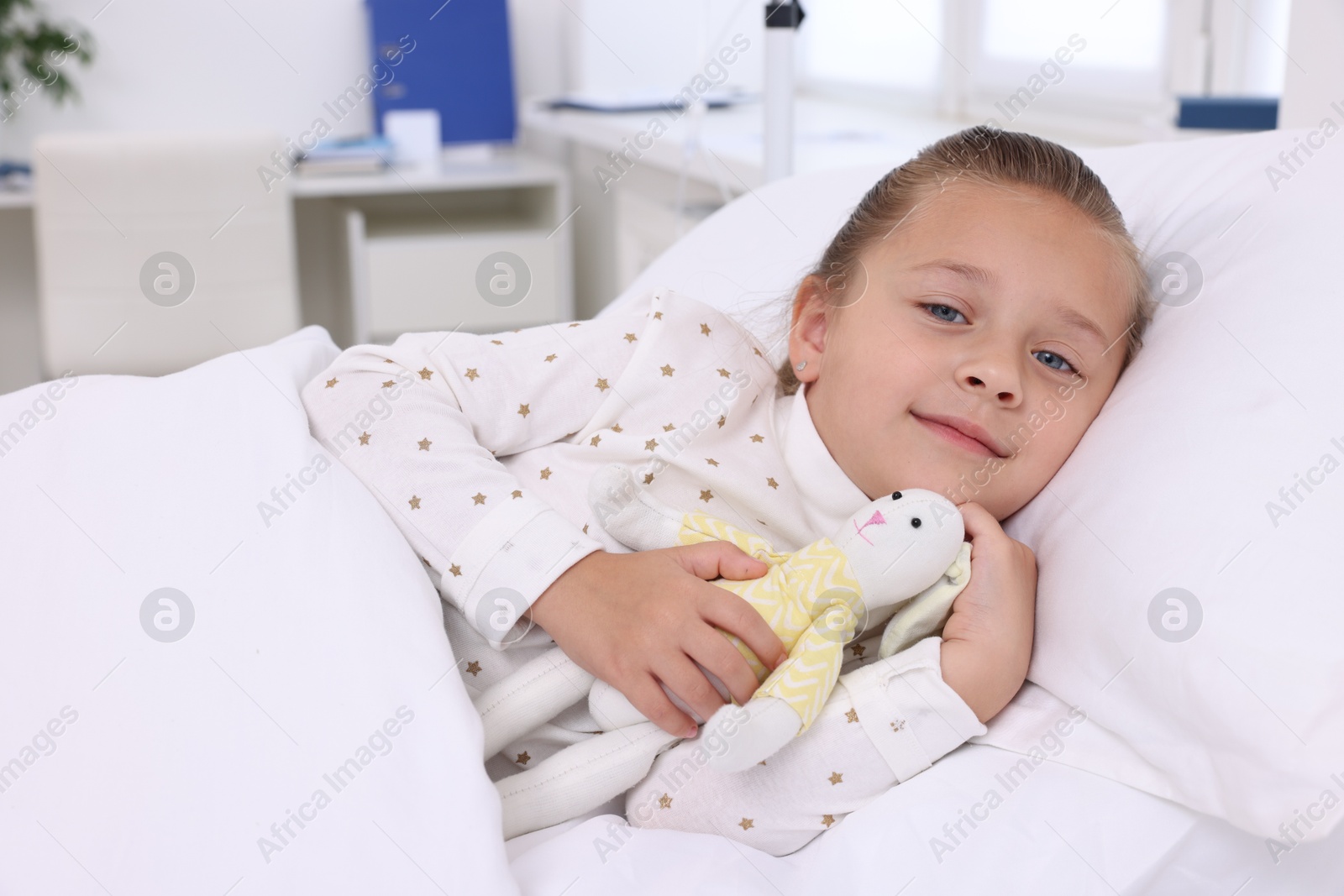 Photo of Cute little girl with toy bunny on bed in hospital