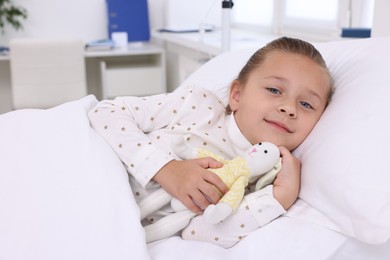 Cute little girl with toy bunny on bed in hospital