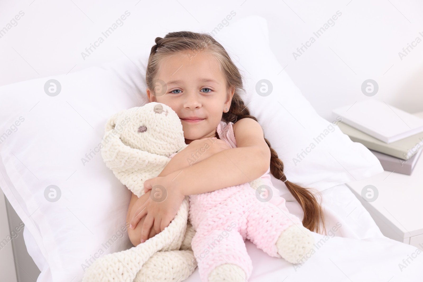 Photo of Cute little girl with toy bunny on bed in hospital