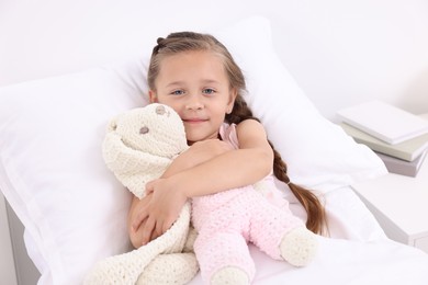 Cute little girl with toy bunny on bed in hospital