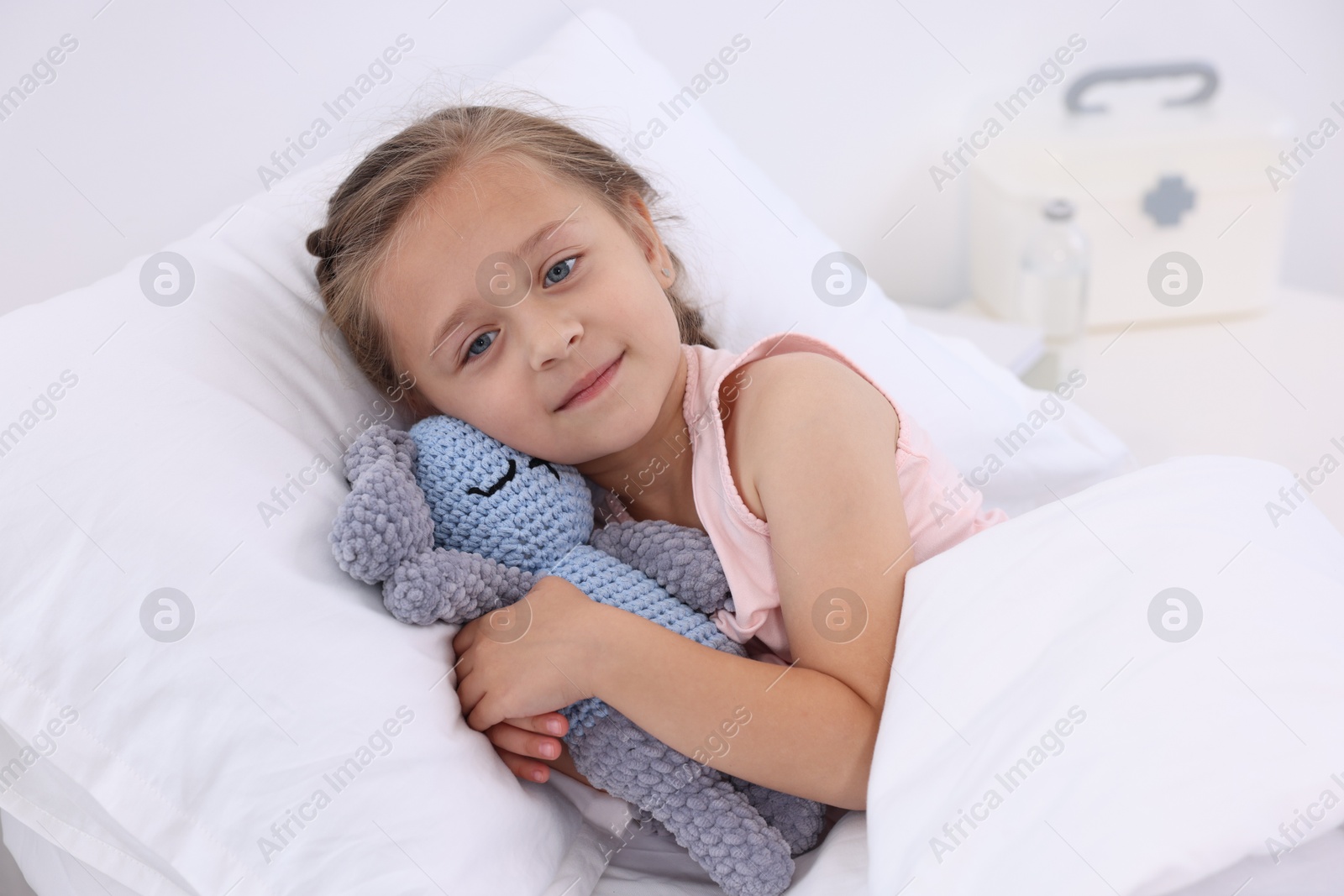 Photo of Cute little girl with toy bunny on bed in hospital