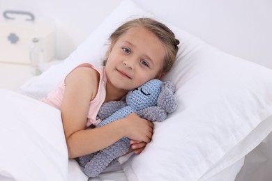 Cute little girl with toy bunny on bed in hospital