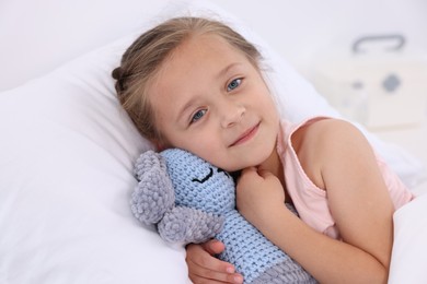 Photo of Cute little girl with toy bunny on bed in hospital