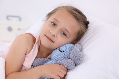 Cute little girl with toy bunny on bed in hospital