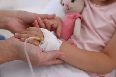 Photo of Mother and her little daughter with IV drip on bed in hospital, closeup