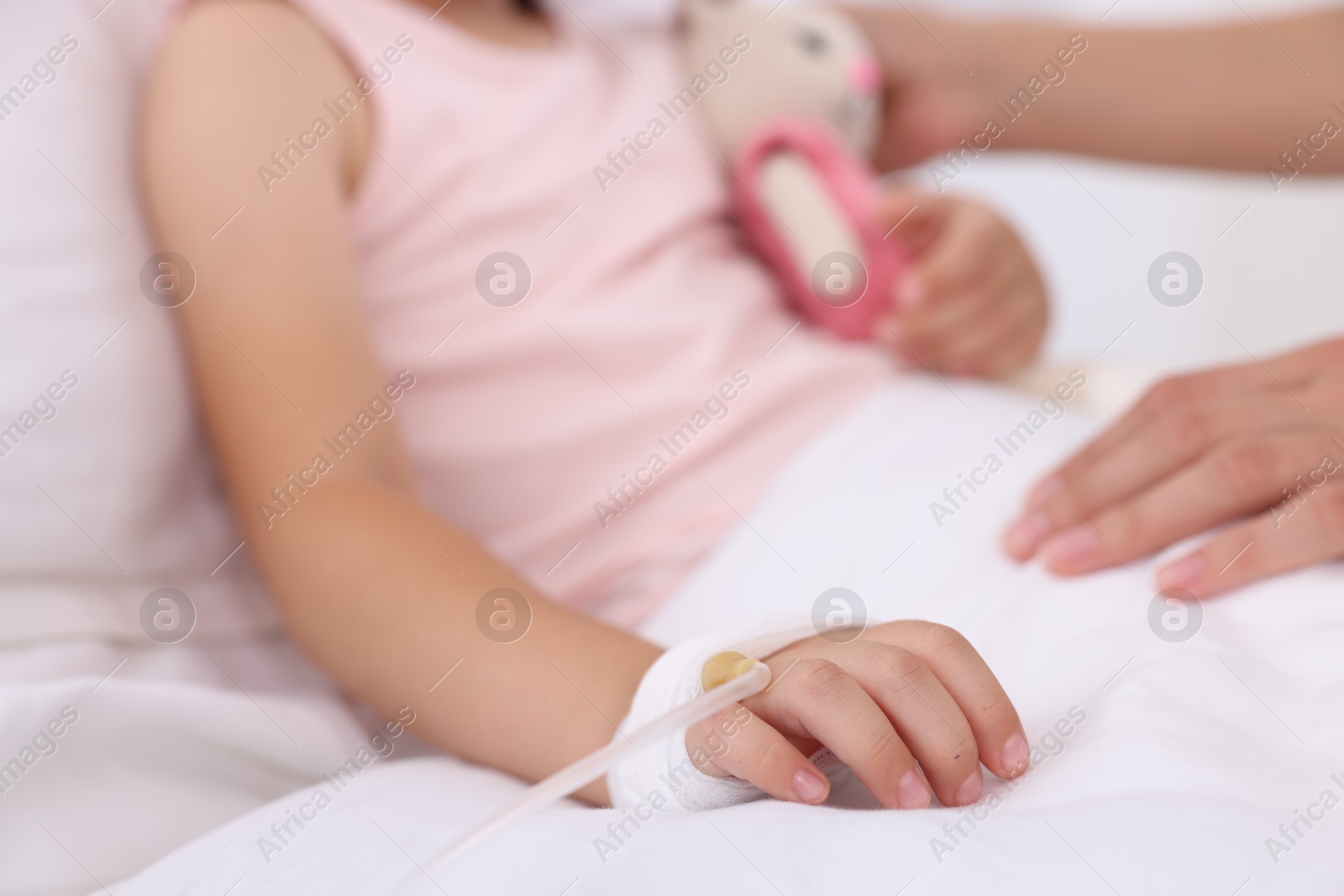 Photo of Mother and her little daughter with IV drip on bed in hospital, closeup