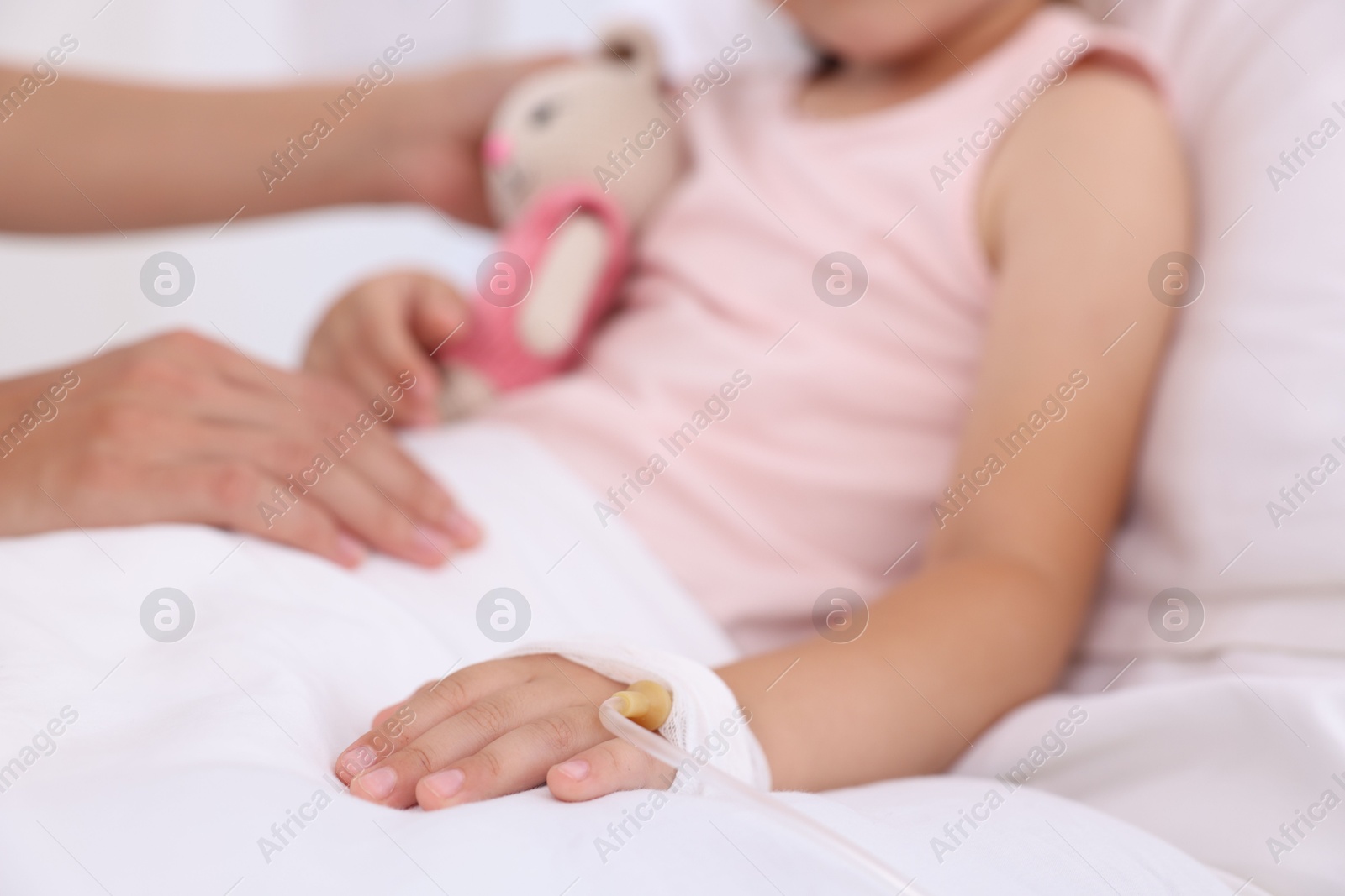 Photo of Mother and her little daughter with IV drip on bed in hospital, closeup