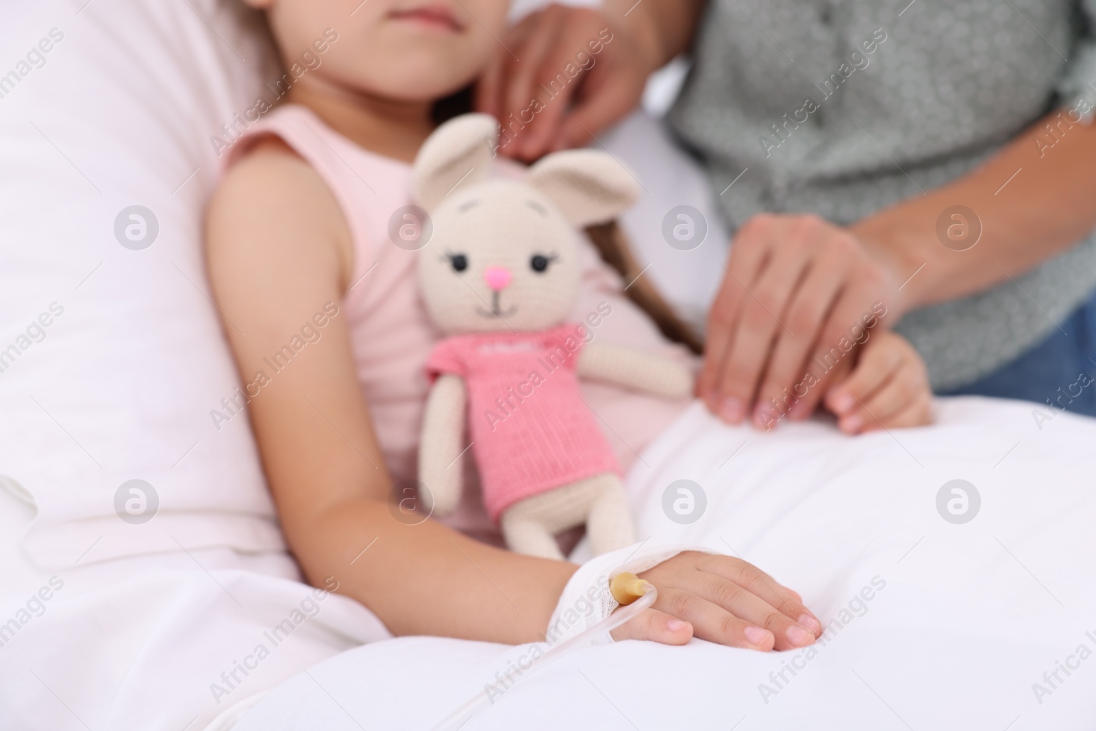 Photo of Mother and her little daughter with IV drip on bed in hospital, closeup