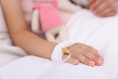 Photo of Mother and her little daughter with IV drip on bed in hospital, closeup