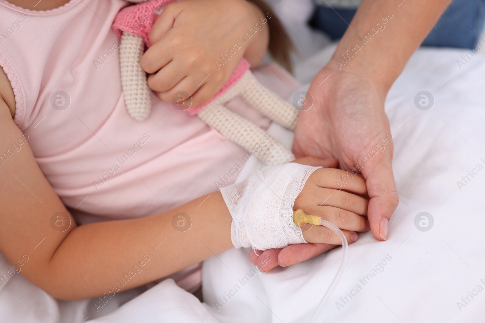 Photo of Mother and her little daughter with IV drip on bed in hospital, closeup