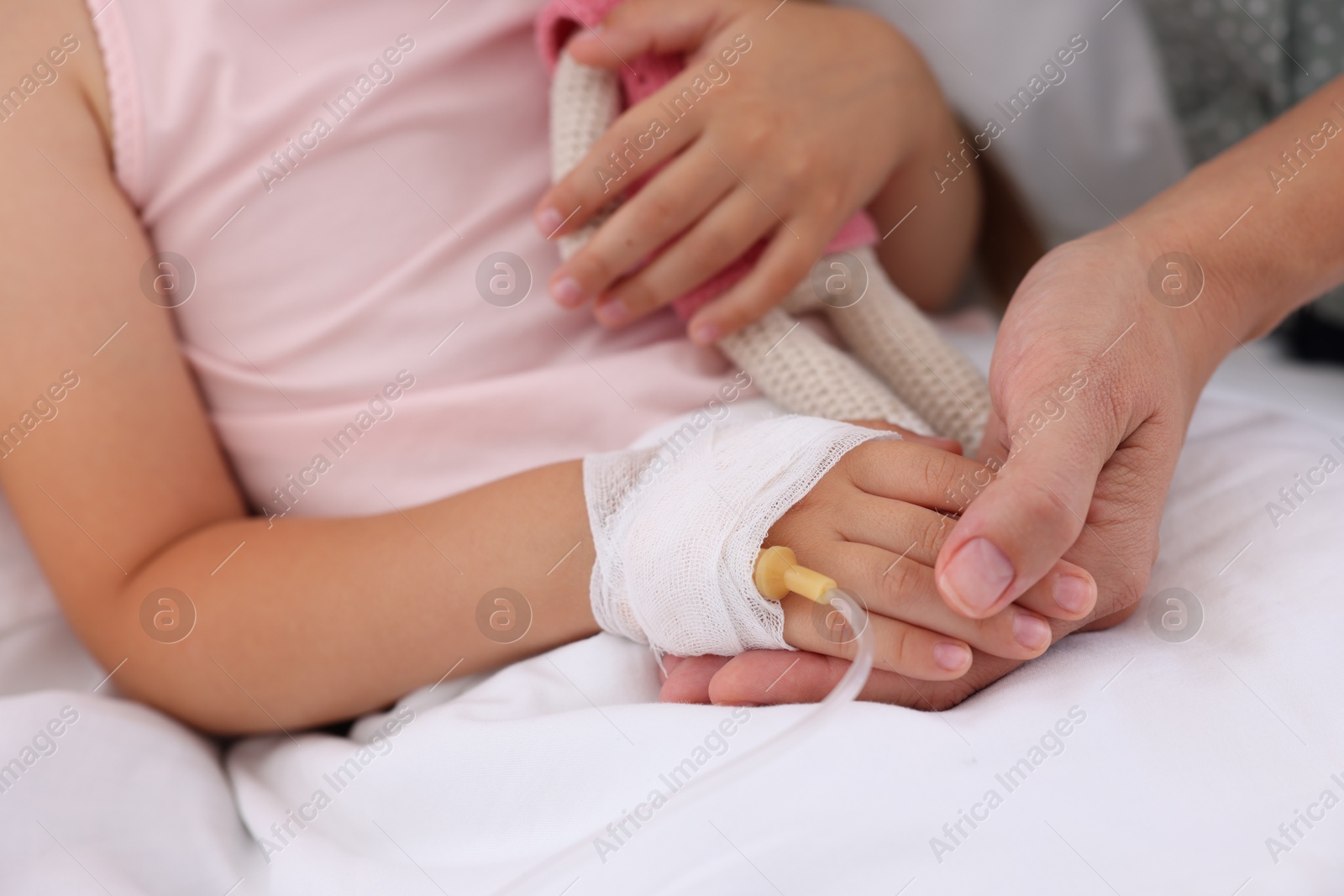 Photo of Mother and her little daughter with IV drip on bed in hospital, closeup