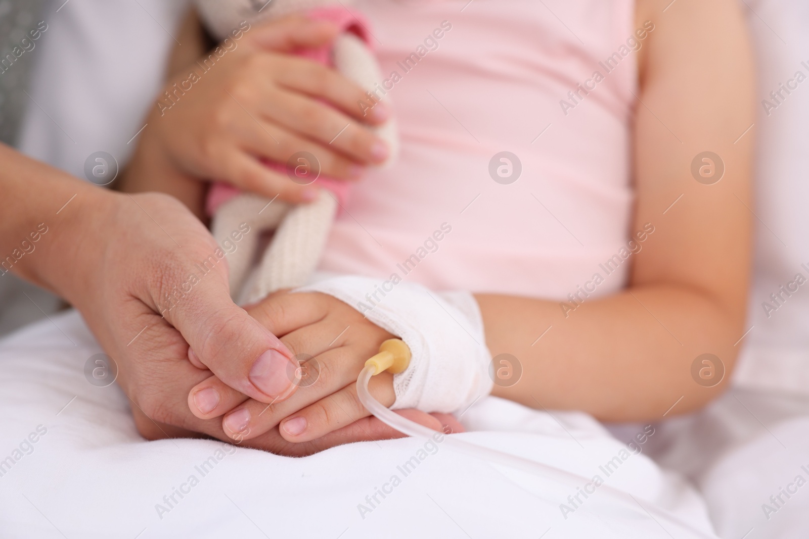 Photo of Mother and her little daughter with IV drip on bed in hospital, closeup