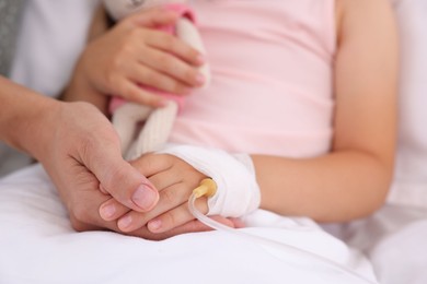 Photo of Mother and her little daughter with IV drip on bed in hospital, closeup