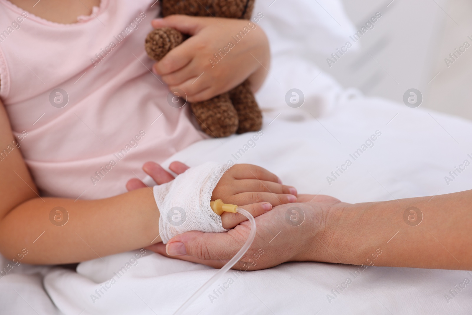 Photo of Mother and her little daughter with IV drip on bed in hospital, closeup